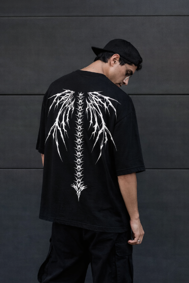 Person wearing a black t-shirt with a white skeleton design on the back against a dark wall.