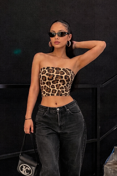 Woman wearing a leopard print top and black jeans standing against a black background.